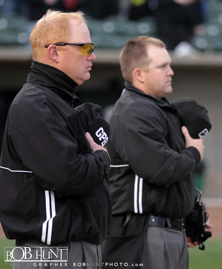 Midwest League umpires stand at attention during the National Anthem before the start of the game